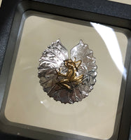 Frog on lily pad pendant, 30mm, rhodium plated, .925 sterling silver, 18Kt gold plating on frog. Sold with an 18” sterling silver chain. Authorized reproduction of an original museum quality Rainforest Design®️handcrafted shell cameo, carved in Panama by a master Wounaan Indian artist. Part of the proceeds go to the artist whose signature appears on the reverse. The Panama Golden Frog or Rana Dorada, is now extinct in the wild,